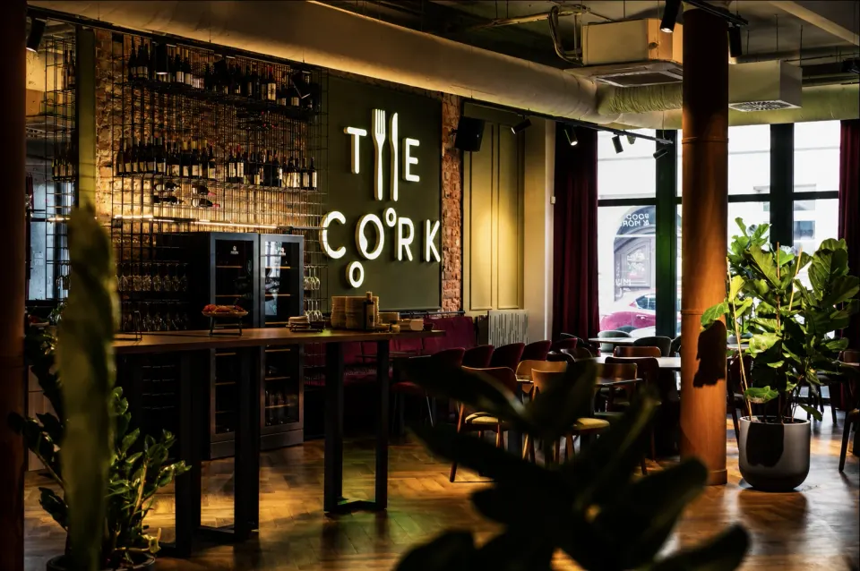 Sala The Cork: podświetlony napis The Cork, regał z winem i stoliki przy oknach