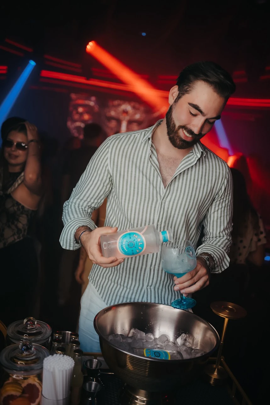 Gin Malfy nalewany do kieliszka z lodem w SiSi, za nim bawiący się goście